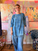 Load image into Gallery viewer, Front view of a West African indigo-dyed shirt with side slits and fringed lower edge, modeled indoors
