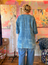 Load image into Gallery viewer, Back view of a West African indigo-dyed shirt with side slits and fringed lower edge, modeled indoors