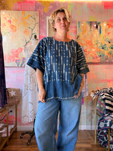 Load image into Gallery viewer, Back view of a deep blue West African indigo-dyed shirt with contrasting linear pattern and fringed hem, modeled indoors