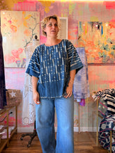 Load image into Gallery viewer, Alternate front view of a deep blue West African indigo-dyed shirt with wide sleeves and fringed hem, modeled indoors