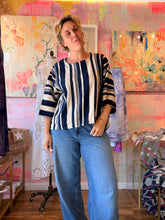 Load image into Gallery viewer, Front view of a West African indigo-dyed shirt with bold navy and cream vertical stripes and wide sleeves, modeled indoors