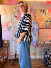 Load image into Gallery viewer, Side view of a West African indigo-dyed shirt with bold contrasting stripes and wide sleeves, modeled indoors