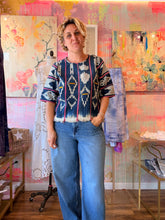 Load image into Gallery viewer, Front view of a deep navy West African indigo-dyed shirt with light geometric motifs, pink stripes, and fringed hem, modeled indoors
