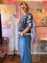 Load image into Gallery viewer, Side view of a deep navy West African indigo-dyed shirt with light geometric motifs, pink stripes, and fringed hem, modeled indoors