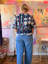 Load image into Gallery viewer, Back view of a deep navy West African indigo-dyed shirt with light geometric motifs, pink stripes, and fringed hem, modeled indoors