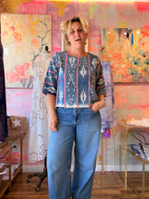 Load image into Gallery viewer, Front view of a deep blue West African indigo-dyed shirt with pale vertical motifs, pink accent stripes, and fringed hem, modeled indoors
