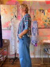 Load image into Gallery viewer, Side view of a West African indigo-dyed shirt with pale vertical motifs, pink accent stripes, and patterned short sleeves, modeled indoors