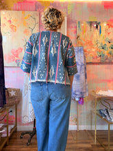 Load image into Gallery viewer, Back view of a deep blue West African indigo-dyed shirt with pale vertical motifs, pink accent stripes, and fringed hem, modeled indoors