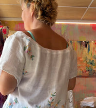 Load image into Gallery viewer, Model wearing a loose white gauzy dress tunic with floral embroidery and a pink drawstring neckline