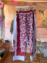 Load image into Gallery viewer, Front view of berry and lavender floral tablecloth pants with elastic waistband hanging on a hanger