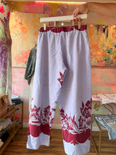 Load image into Gallery viewer, Back of vintage tablecloth pants in lavender-white with a berry-red floral border at the hems