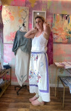 Load image into Gallery viewer, Front of white tablecloth pants with a lavender side stripe and blue and red floral print on a model
