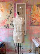 Load image into Gallery viewer, Front view of an ivory tank top made from a vintage tablecloth, with dark scroll embroidery along the hem and adjustable straps.