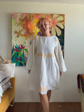 Load image into Gallery viewer, Modeled Angle Wing dress with wide neckline, flared skirt, and yellow cross-stitching on vintage linen.