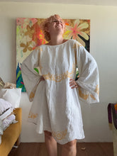 Load image into Gallery viewer, Front view of Caramiya Angle Wing dress in pale vintage linen with yellow cross-stitching and flowing sleeves.